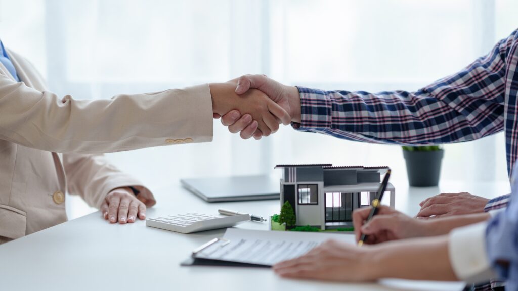 A couple sign a contract and shake the hand of an estate agent as they agree to purchase a house.