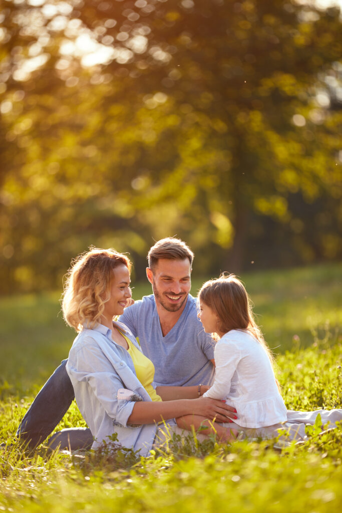 A young happy couple and their daughter relax in a field on a sunny day.