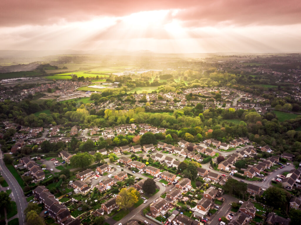 An aerial view of the sun bursting through the clouds over a large residential area.