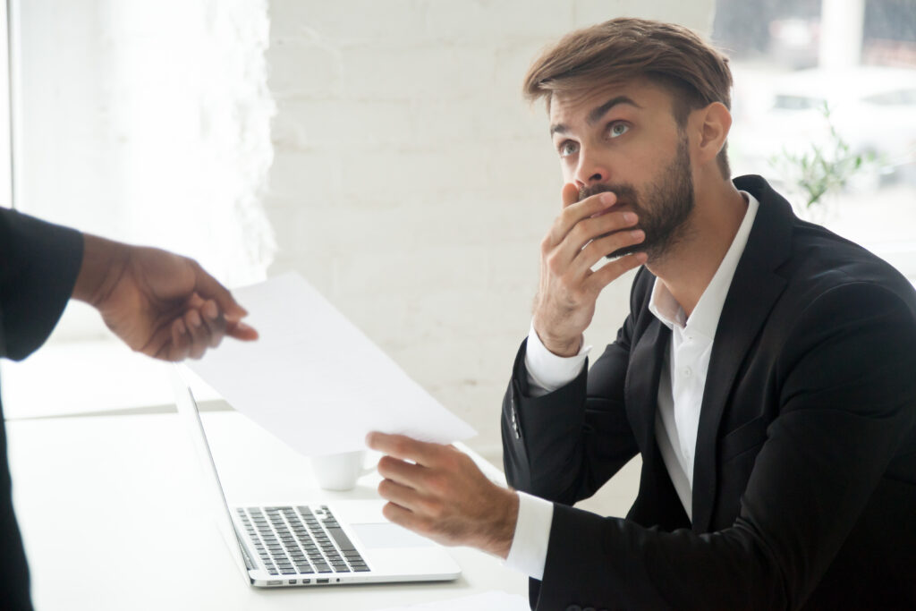 An male employee appears to be nervous as he is handed a dismissal notice by a colleague.