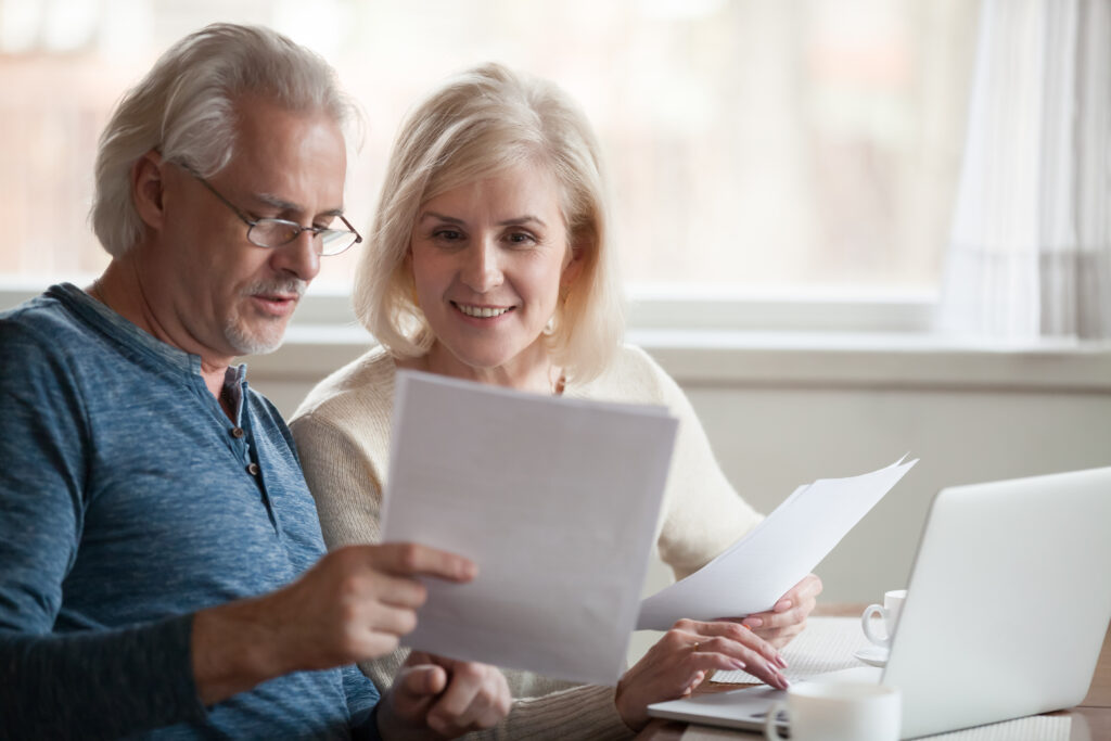 A happy senior couple read through documents together while sitting at a table.