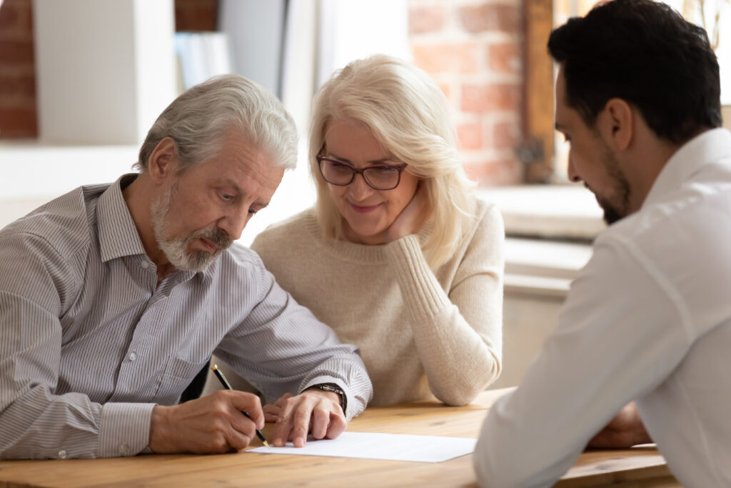 A happy senior couple sign a document with a male solicitor.