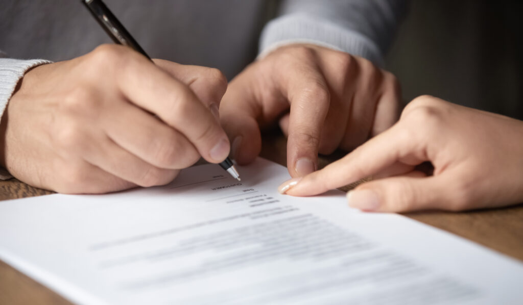 A closeup of a female solicitor guiding a male client on where to write his signature on a contract.