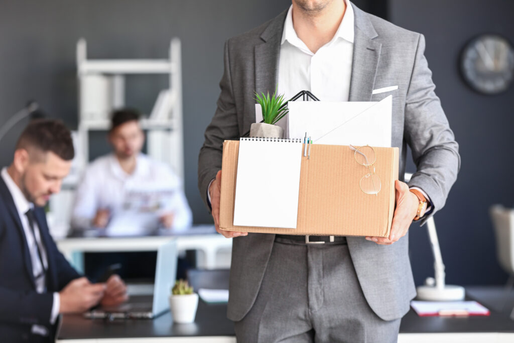 A man, who has been fired, walks through the office with a box of his personal possessions.