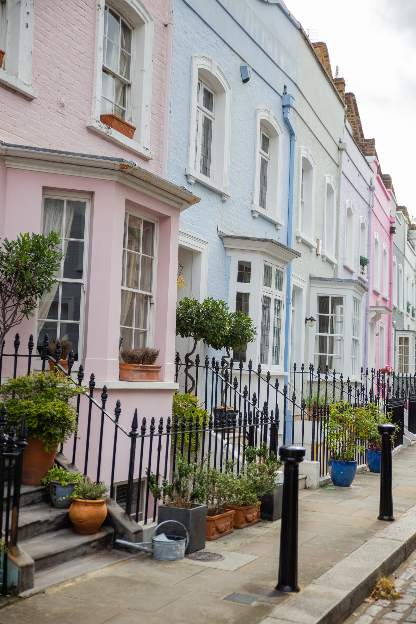 A row of colourful English terraced houses with black hand rails and potted plants.