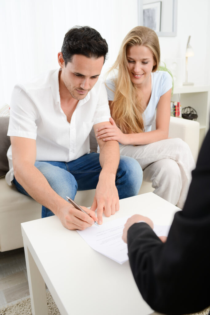 A happy young couple sign a legal document in their home.