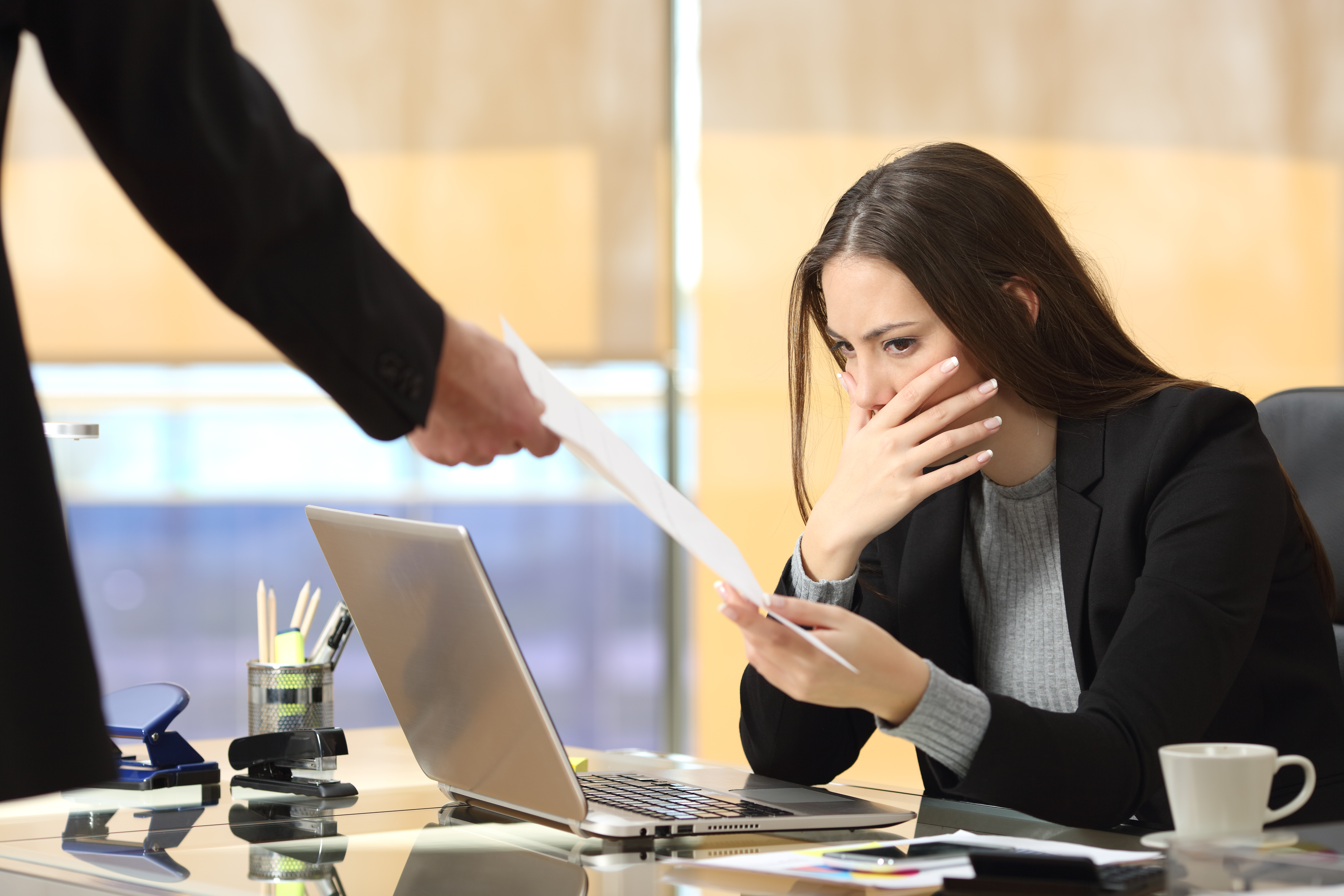 A woman has a worried look on her face as her colleague hands her a dismissal notice.