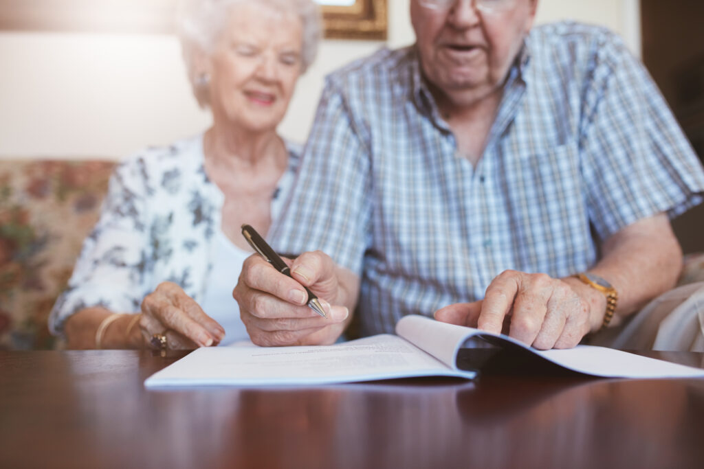 A smiling elderly couple sit on the sofa and read through a booklet of legal documents.