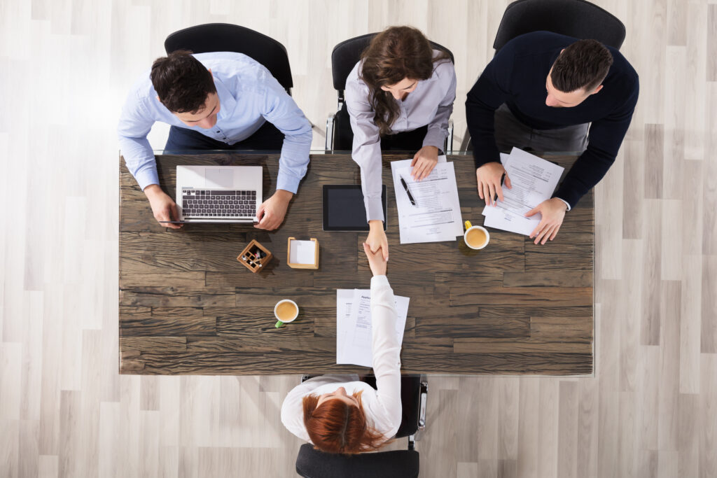 An aerial view of a group of three recruiters greeting and shaking hands with a female interviewee.