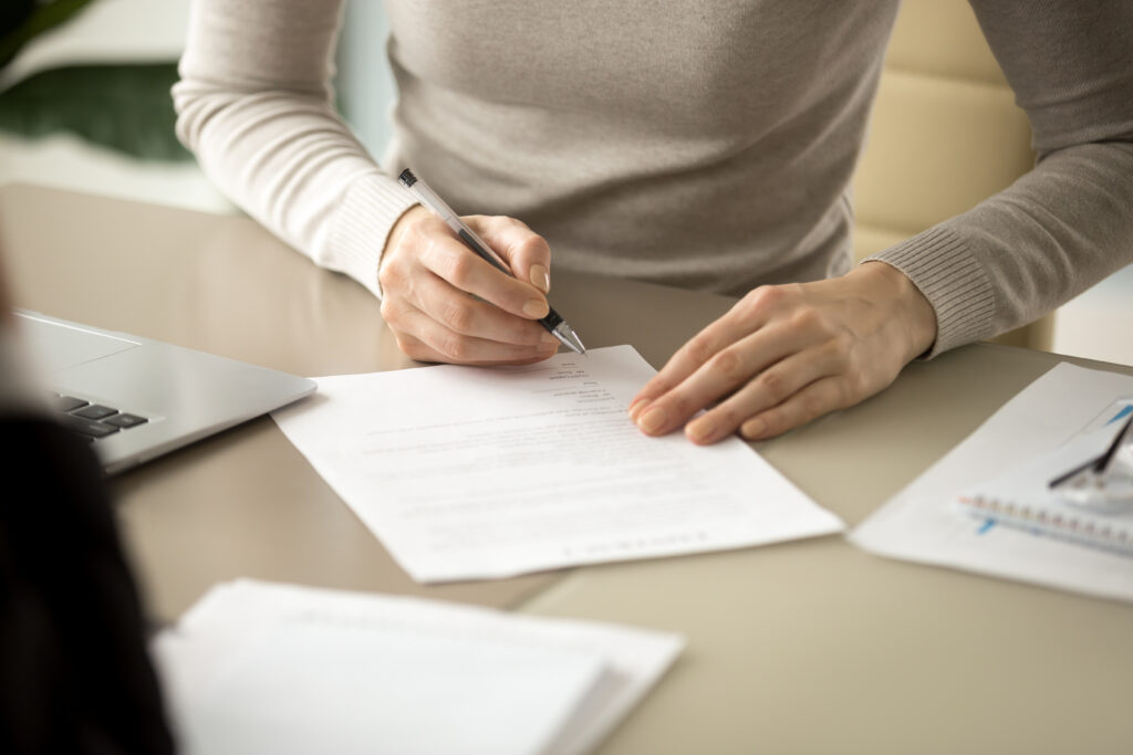 A closeup of a woman signing a document at her desk.