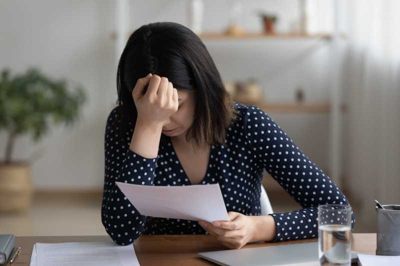 A woman looks distraught and holds her head in her hand as she reads an unjustified demotion notice.