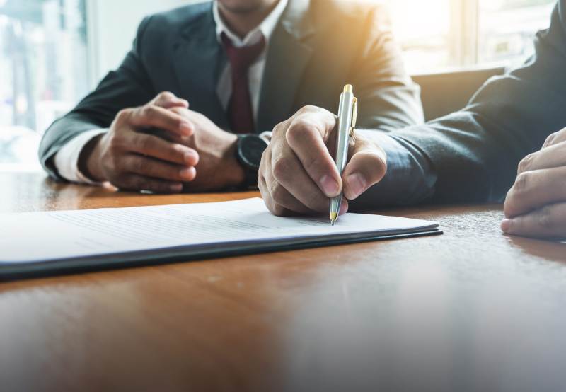 A closeup of a businessman signing a document in a meeting.