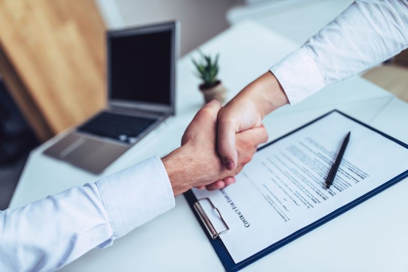 A new employee shakes the hand of a businessman after signing an employment contract.