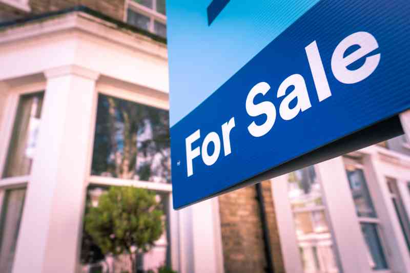 A closeup of an estate agent's "for sale" sign outside of a residential property.