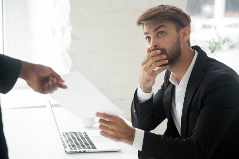 An male employee appears to be concerned as he is handed a dismissal notice by a colleague.