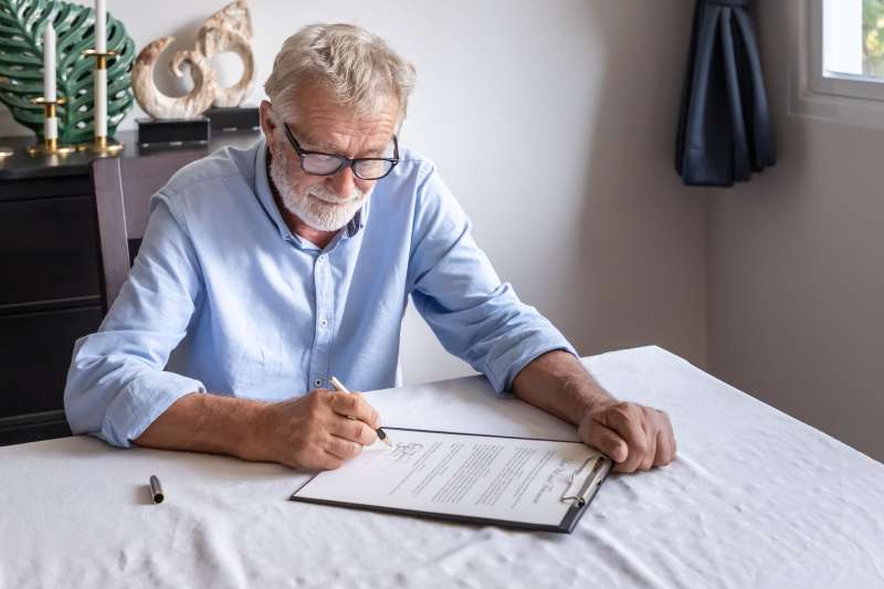 An elderly man sits at his dining room table and reviews his will